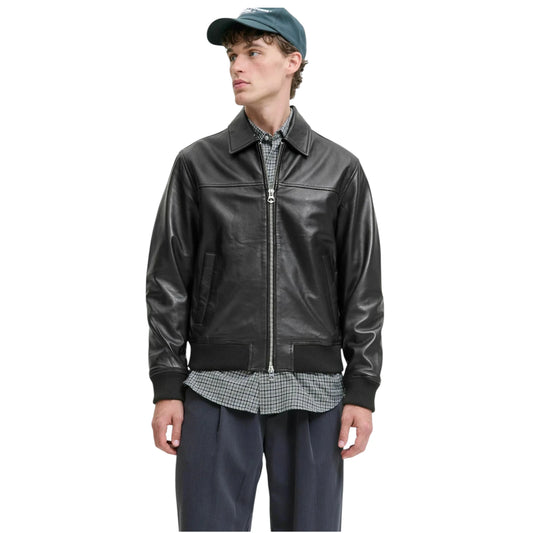 Man wearing a black leather jacket, plaid shirt, and cap on a white background